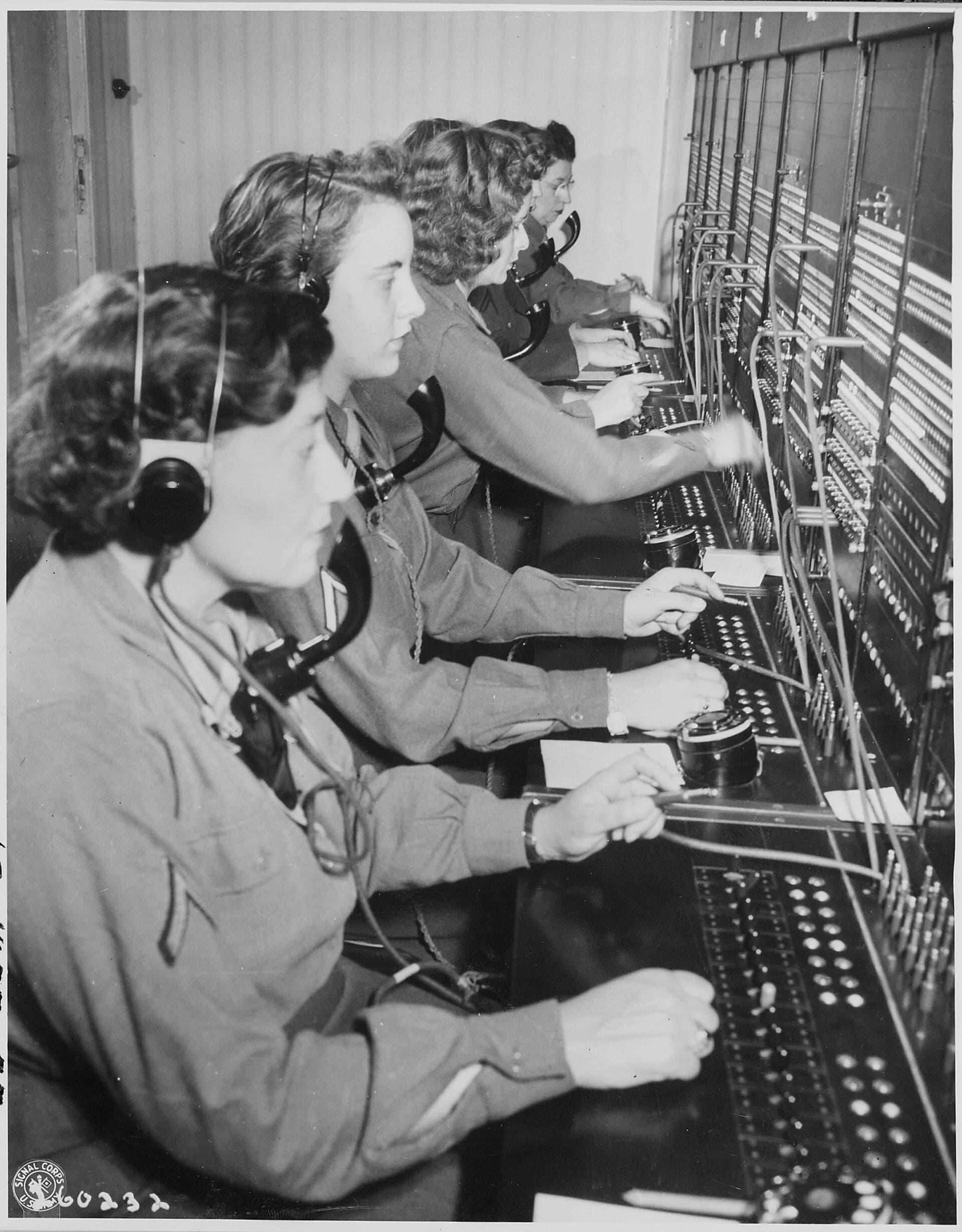 Army telephone operators at a large switchboard, wearing headsets and connecting calls by hand.